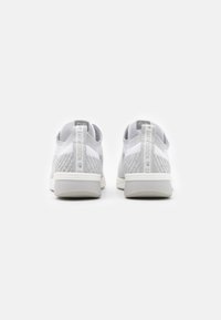 Zapatillas de punto en gris y blanco con un tacón bajo, que presentan un patrón texturizado, una tira de agarre y una suela de goma lisa.