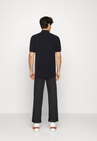 Polo noir à manches courtes avec un col classique, associé à un pantalon foncé retroussé et des baskets blanches avec des accents marron.