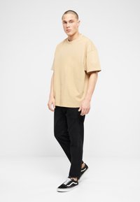 Béžové oversized tričko s krátkymi rukávmi, skombinované s čiernymi nohavicami rovného strihu a čiernymi teniskami s bielymi akcentmi. Jednoduchý a ležérny outfit.
