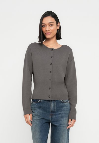 Cardigan gris en maille côtelée avec col rond et fermeture à boutons. Comprend des manches longues et une taille cintrée. Porté avec un jean bleu.