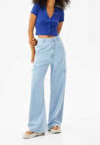 Hellblaue, weit geschnittene Cargo-Hosen mit großen Seitentaschen, strukturiertem Stoff und hoher Taille; kombiniert mit einem eng anliegenden, dunkelblauen Cropped-Top.