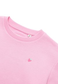 Różowa bluza z okrągłym dekoltem, teksturowaną tkaniną oraz małym haftowanym akcentem truskawki na lewej stronie klatki piersiowej.