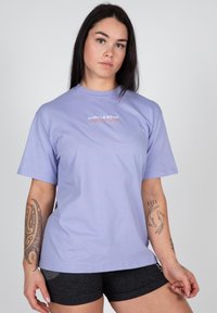 Light purple short-sleeve t-shirt made of cotton, featuring a white and orange printed logo on the chest. Smooth texture, relaxed fit.