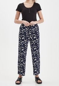 Svart ribbad topp med kort ärm och tre knappar, tillsammans med marinblå byxor med blommönster och vida ben. Slät tyg, avslappnad passform, med platta sandaler.