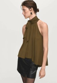 Olive green halter top with a knotted neck and draped fabric. Paired with a black leather mini skirt featuring an asymmetrical hem.