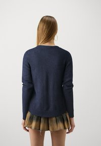 Mörkblå stickad tröja med långa ärmar och ribbat avslut, i kombination med en plisserad, tie-dye kjol. Slät textur, avslappnad passform.