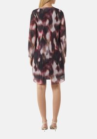 Fältetes Kleid mit einem mehrfarbigen abstrakten Muster in verschiedenen Schattierungen von Pink, Schwarz und Creme. Lange Ärmel und ein runder Ausschnitt.