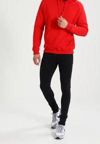 Czerwona bluza z kapturem i kieszenią kangurką, połączona z czarnymi obcisłymi dżinsami i szarymi trampkami z białymi akcentami.