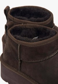 Brązowe zamszowe botki za kostkę z miękką podszewką z owczej wełny, wykończone materiałowym mankietem i wzmocnionym szwem, z niską platformą.