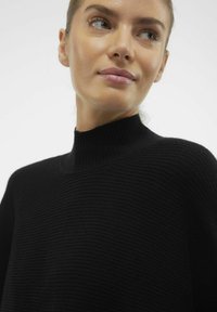 Črna rebrasta pulover s turtleneck izrezom, z visokim ovratnikom, subtilno teksturo in prilegajočo silhueto, ki se osredotoča na preprostost in udobje.
