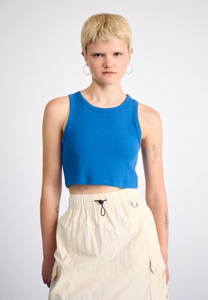 Blå ribbet crop-top med rund halslinning, parret med en beige cargo-nederdel med snor i taljen og sidelommer. Modellen har kort hår.