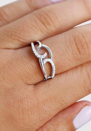 Silver ring with a wavy design, featuring small clear gemstones along one side. Positioned on a hand with a light skin tone.