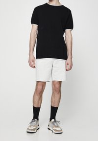 T-shirt noire à manches courtes avec bord blanc, associé à un short gris clair. porté avec des chaussettes noires et des baskets multicolores.