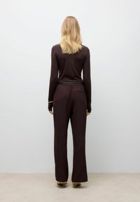 Maglietta marrone a maniche lunghe abbinata a pantaloni larghi marrone scuro. Texture liscia e dettagli di design sottili, inclusi accenti sartoriali.