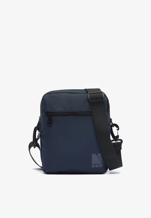 Torba na rame mornarsko plave boje s prednjim džepom sa zatvaračem i podesivim crnim remenom, s malim geometrijskim logotipom u donjem desnom kutu.