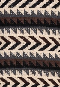 Tissu beige, présentant un motif en zigzag en noir, marron foncé et gris. La texture est tricotée avec des points visibles et une épaisseur de fil variable.
