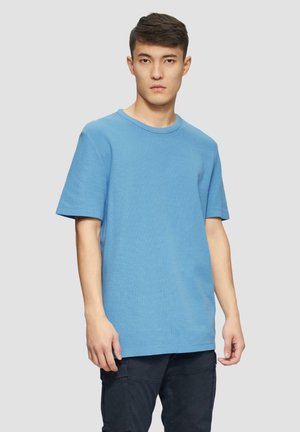 Short-sleeve blue crew neck t-shirt in textured fabric, relaxed fit. Worn with dark cargo pants, featuring a straight silhouette.