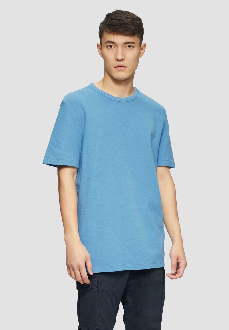 Blauwe t-shirt met korte mouwen en ronde hals in een gestructureerde stof, met een ontspannen pasvorm. Draagt met donkere cargo broeken, met een rechte silhoutte.