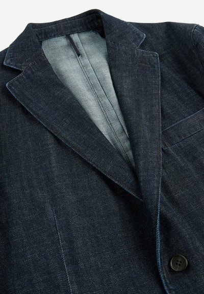 Czarna dżinsowa marynarka z ostrym kołnierzem, z pojedynczym zapięciem na guzik, o fakturowanej tkaninie i kontrastowym jasnoniebieskim podbiciu. Posiada kieszeń na piersi.