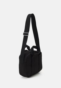 Czarna, prostokątna torebka na ramię z regulowanym szerokim paskiem, dwoma górnymi uchwytami oraz przednią kieszenią na klapę na białym tle.
