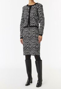 Set di cardigan e gonna a maglia con motivo zebratato in bianco e nero, abbinato a stivali neri in pelle al ginocchio, con una silhouette aderente.