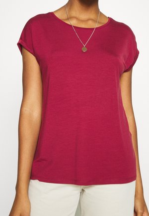 Woman wearing a plain short-sleeve red t-shirt and white pants, with a silver necklace featuring a round pendant.