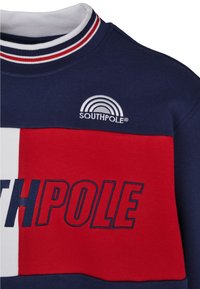 Námořnická a červená svetr s bílým límcem. Na hrudi se nachází vyšívaný text "SOUTHPole" a logo s duhou.