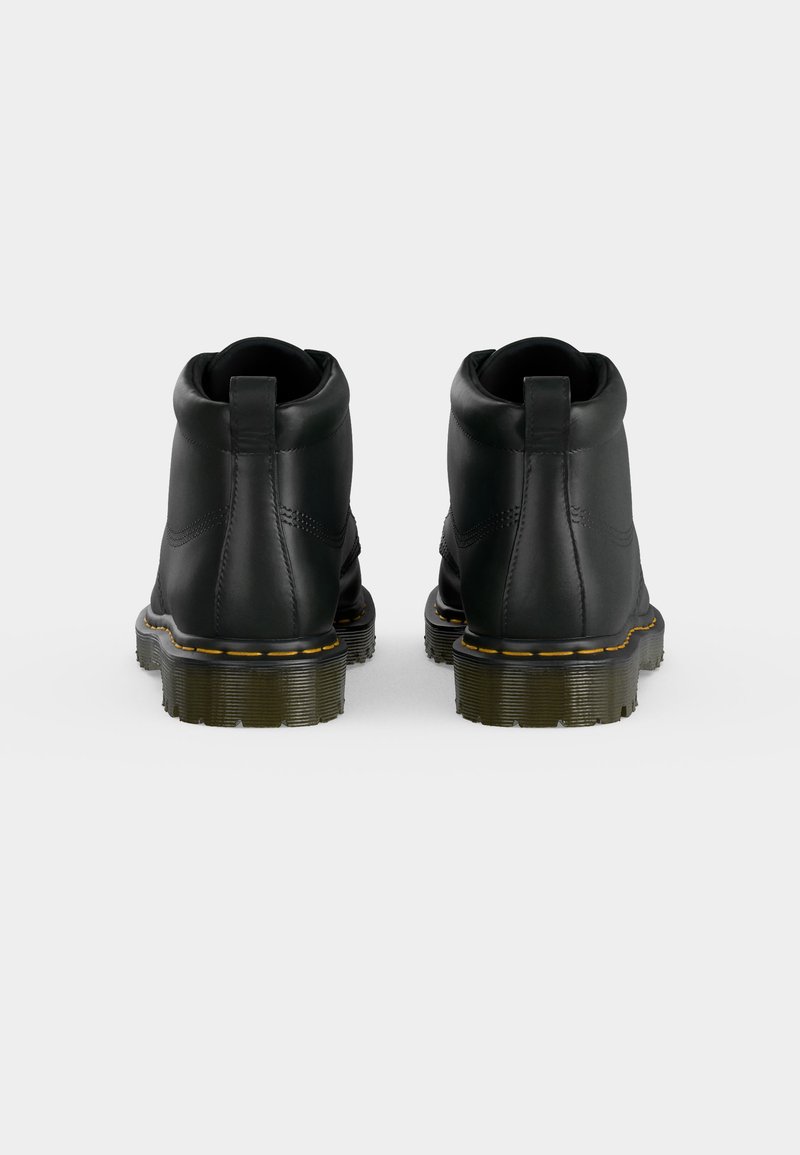 Paar schwarze Lederstiefel, von hinten gezeigt, mit gelben Nähten über dicken Gummisohlen, vor einem schlichten weißen Hintergrund.