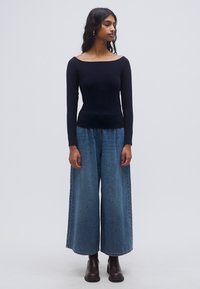 Μαύρο μακρυμάνικο τοπ σε συνδυασμό με μπλε τζιν παντελόνι φαρδιάς γραμμής. Το σύνολο διαθέτει εφαρμοστή σιλουέτα και απαλή υφή.