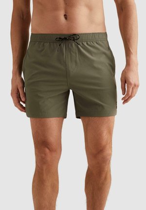 Mužský trup a nohy v olivovo zelených plaveckých šortkách s elastickým pásom a čiernym sťahovacím šnúrikom na jednofarebnom pozadí.