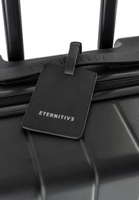 Black hardshell luggage with a textured surface, featuring a handle, zipper, and a black leather luggage tag embossed with "ETERNITIV3."