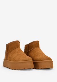 Botas de tobillo de ante marrón con punta redondeada, suela plataforma gruesa y detalles de costura mínimos. Textura suave y color sólido.