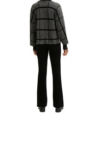 Grauer Pullover mit Muster und schwarzem Gitternetzdesign, langen Ärmeln und gerippten Bündchen, kombiniert mit schwarzen ausgestellten Hosen und schwarzen Schuhen.