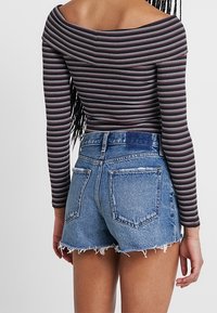Top de manga larga a rayas sin hombros en colores oscuros, combinado con pantalones cortos de mezclilla de tiro alto y desgastados, con dobladillo desflecado.