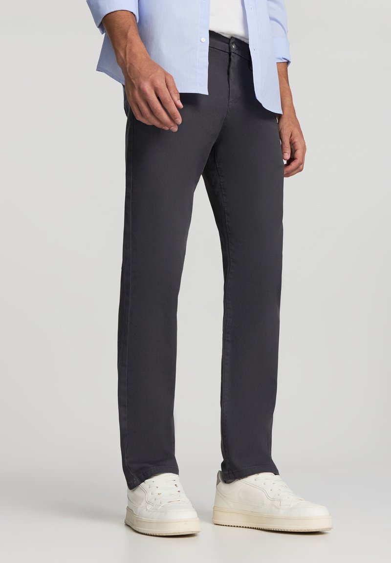 Ciemnoszare chinosy wykonane z bawełnianej mieszanki, z prostym krojem nogawki, subtelnymi detalami przeszyć oraz kieszeniami z przodu. W połączeniu z białymi trampkami.