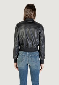 Giacca bomber in pelle nera con polsini e orlo a coste, caratterizzata da una finitura opaca e dal logo "Armani Exchange" in rilievo sul retro.