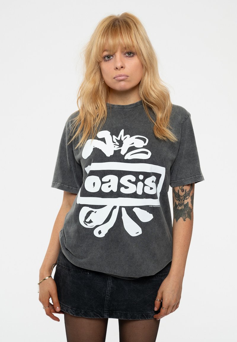 Grey oversized t-shirt featuring a prominent white "oasis" logo and graphic accents. Paired with a black denim skirt, textile texture visible.
