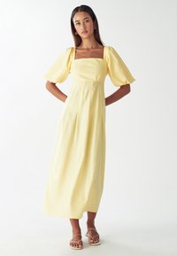 Žlté midi šaty s balónovými rukávmi a štvorcovým výstrihom. Vyrobené z ľahkého materiálu, s priliehavým živôtikom a skladanou sukňou.