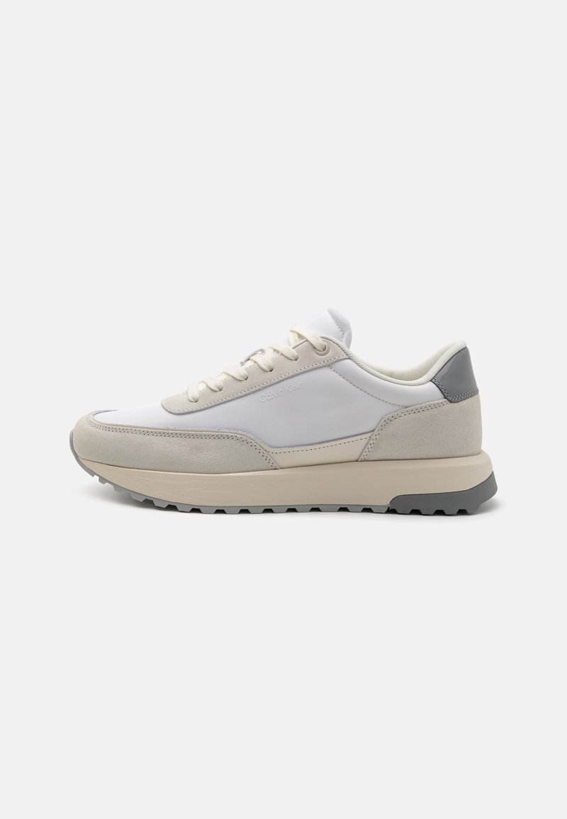 Witte en grijze sneaker met een bovenwerk van suede en glad synthetisch materiaal, ronde neus, vetersluiting aan de voorkant en een gestructureerde rubberen zool. Klassiek atletisch ontwerp.
