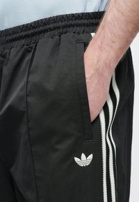 Μαύρο αθλητικό σορτς με ελαστική μέση, πλαϊνές τσέπες και αντίθετες κάθετες ρίγες. Διαθέτει μικρό λευκό λογότυπο στο τελείωμα.