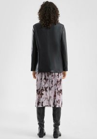 Czarna skórzana kurtka o dopasowanym kroju, zestawiona z lilowo-brązową spódnicą w stylu tie-dye oraz czarnymi kozakami za kolano.