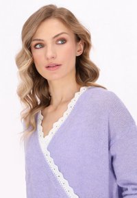 Maglione avvolgente di colore lavanda in morbido materiale lavorato a maglia con scollatura in pizzo bianco a zig zag. Leggero, vestibilità rilassata con maniche lunghe.