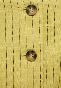 Tessuto giallo con strisce verticali nere, caratterizzato da un bottone marrone e un asola cucita, con una trama strutturata.