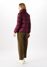 Giacca puffer bordeaux con design a righe verticali, colletto alto e polsini elasticizzati, abbinata a pantaloni verde oliva e sneakers bianche.