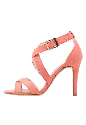 Sandale à talons hauts en daim rose avec des lanières croisées, une boucle dcheville ajustable et un talon incurv. Semelle plate avec texture subtile.