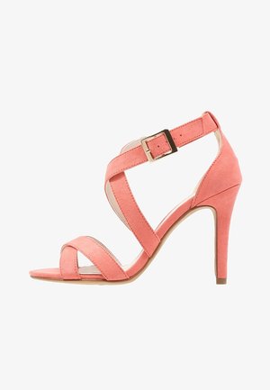 Sandalia de tacón alto en ante rosa con tiras cruzadas, hebilla ajustable en el tobillo y tacón curvado. Suela plana con textura sutil.