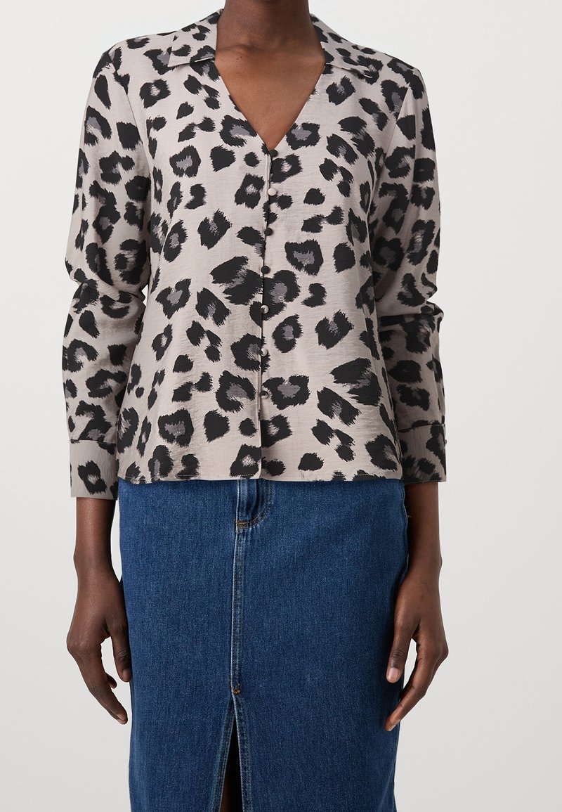 Blouse imprimé léopard en beige clair et noir, avec un col en V, des manches longues, une fermeture à boutons, et une texture lisse. Associée à une jupe en denim.
