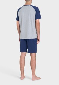 T-shirt grigio a maniche corte con maniche raglan blu navy, abbinato a pantaloni corti blu navy. Tessuto leggero e vestibilità rilassata. Nessun motivo o dettaglio particolare.