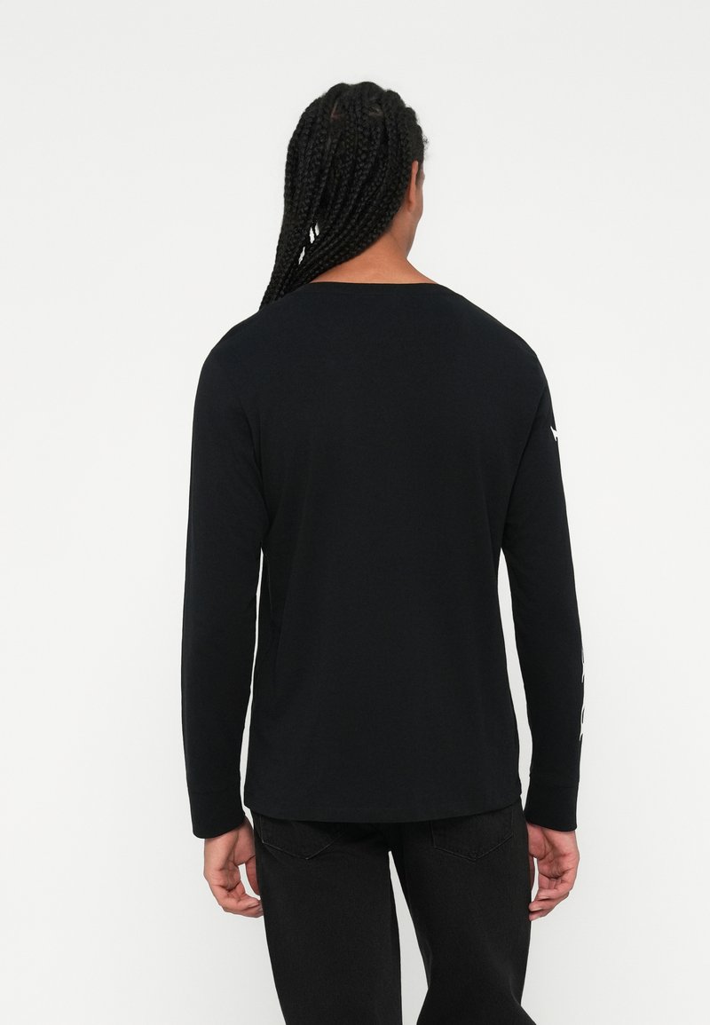 Schwarzes Langarm-T-Shirt aus Baumwolle mit Rundhalsausschnitt und minimalistischer Gestaltung, ergänzt durch gemusterte Akzente an den Ärmeln.