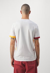 Maillot de sport blanc à manches courtes, avec des accents orange, rouge et jaune. Fabriqué en tissu texturé, avec un détail de logo au dos.